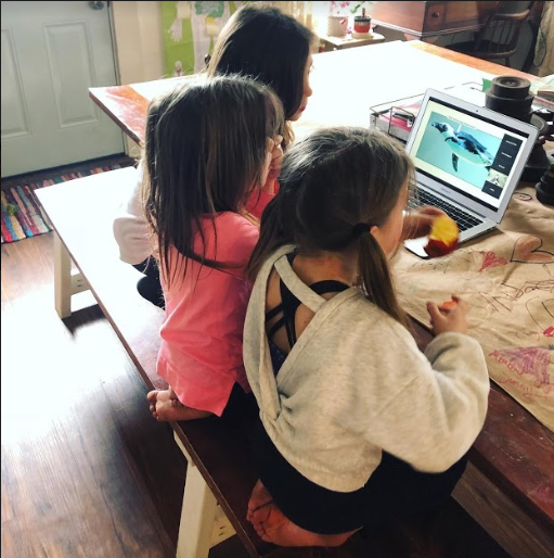 Three young girls sitting at a table watching a penguin video