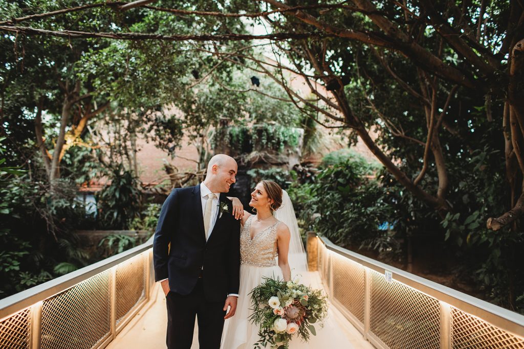 A bride and groom standing on the bridge in the Tropical Rainforest at the National Aviary