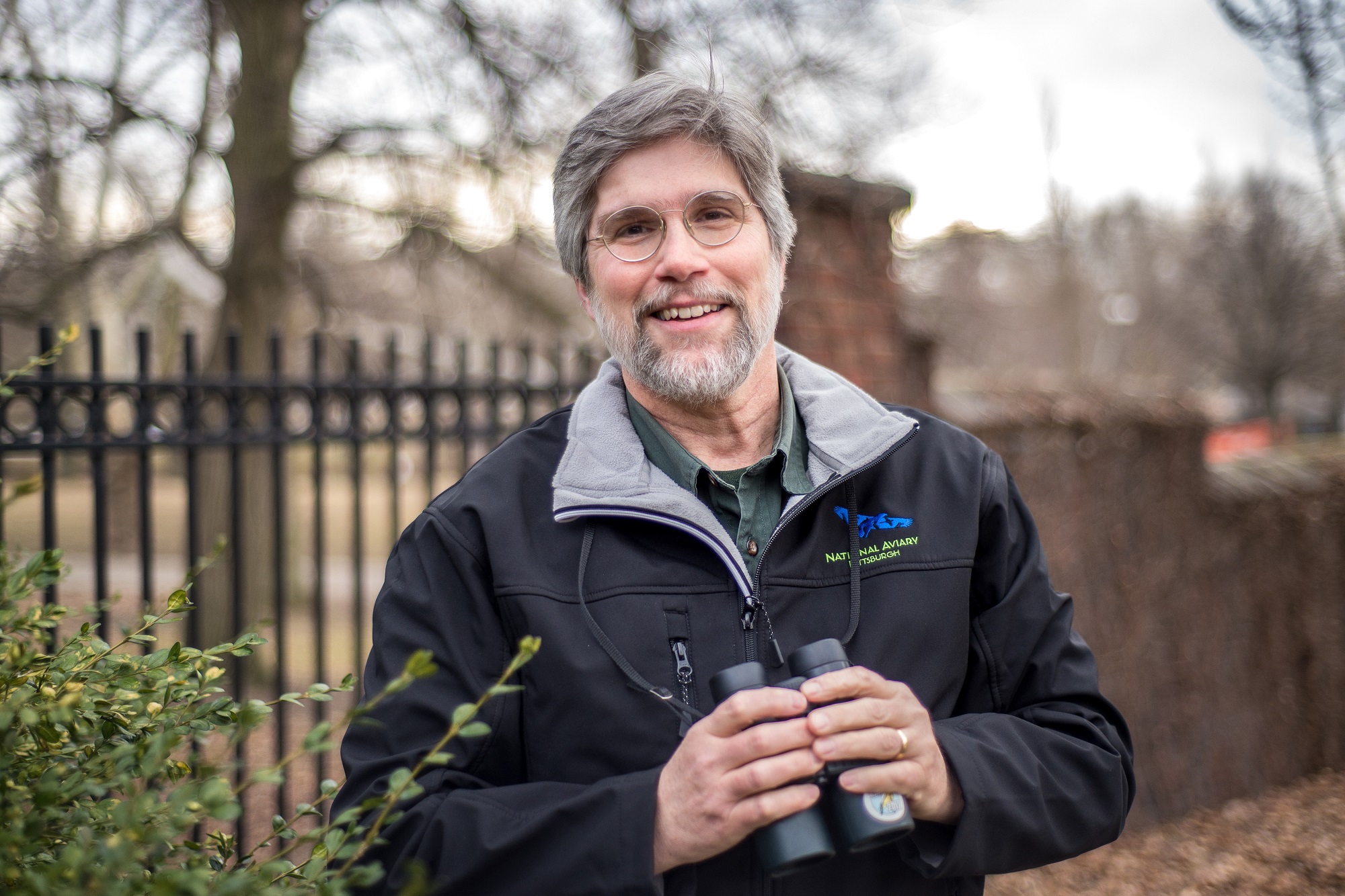 National Aviary Ornithologist Bob Mulvihill smiling holding binoculars