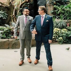 Two grooms holding hands in front of the waterfall in the Tropical Rainforest at the National Aviary