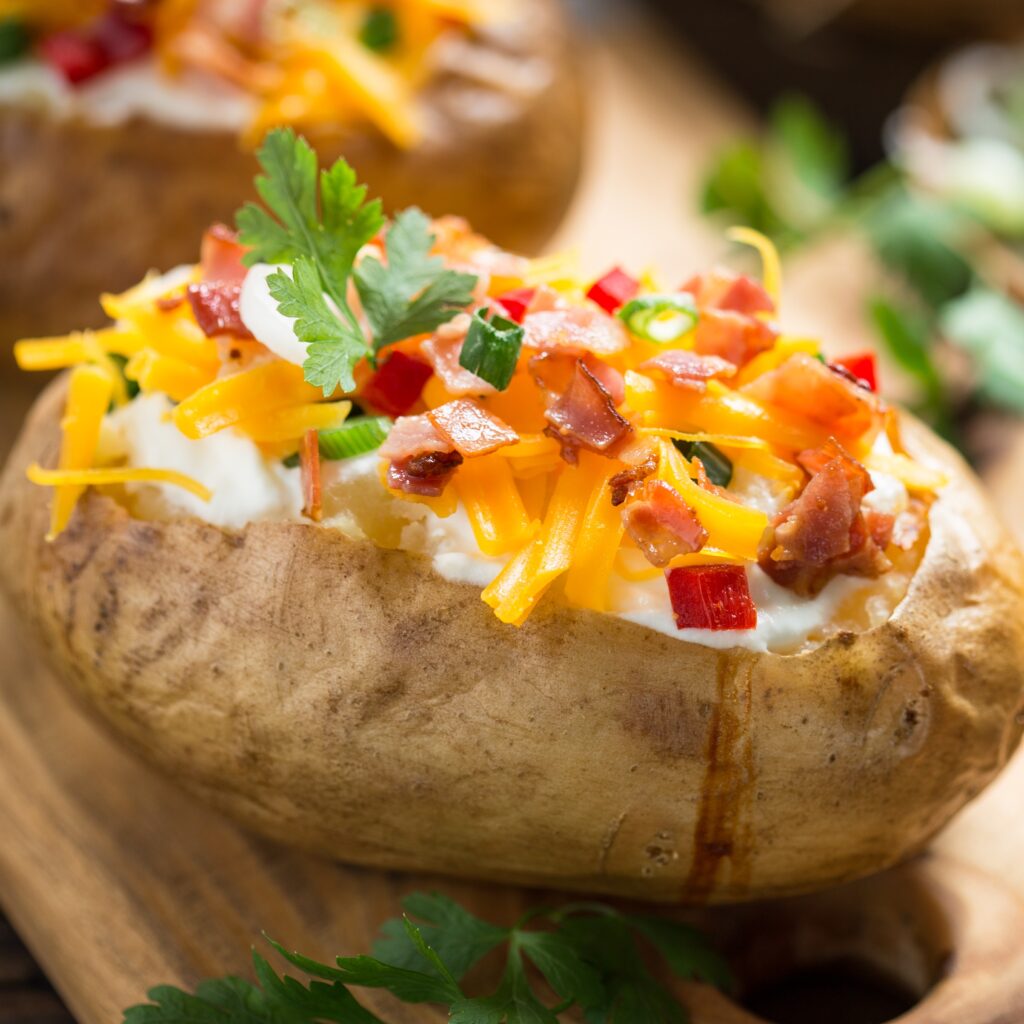 A loaded baked potato topped with sour cream, shredded cheese, bacon bites, and chives.