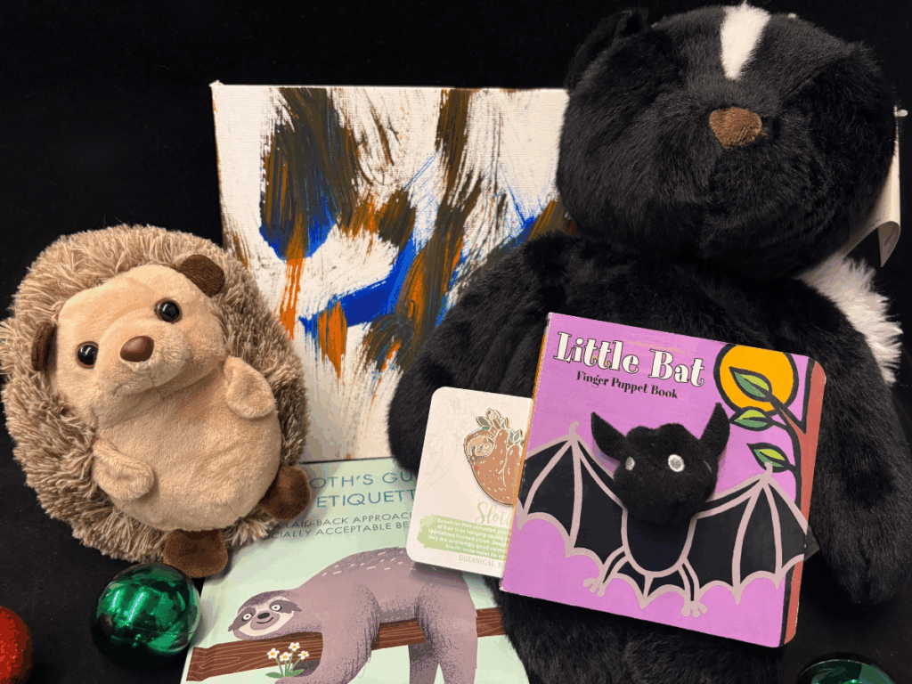 Skunk and hedgehog plush, bat-themed finger puppet book, a sloth pin, and sloth fact book
