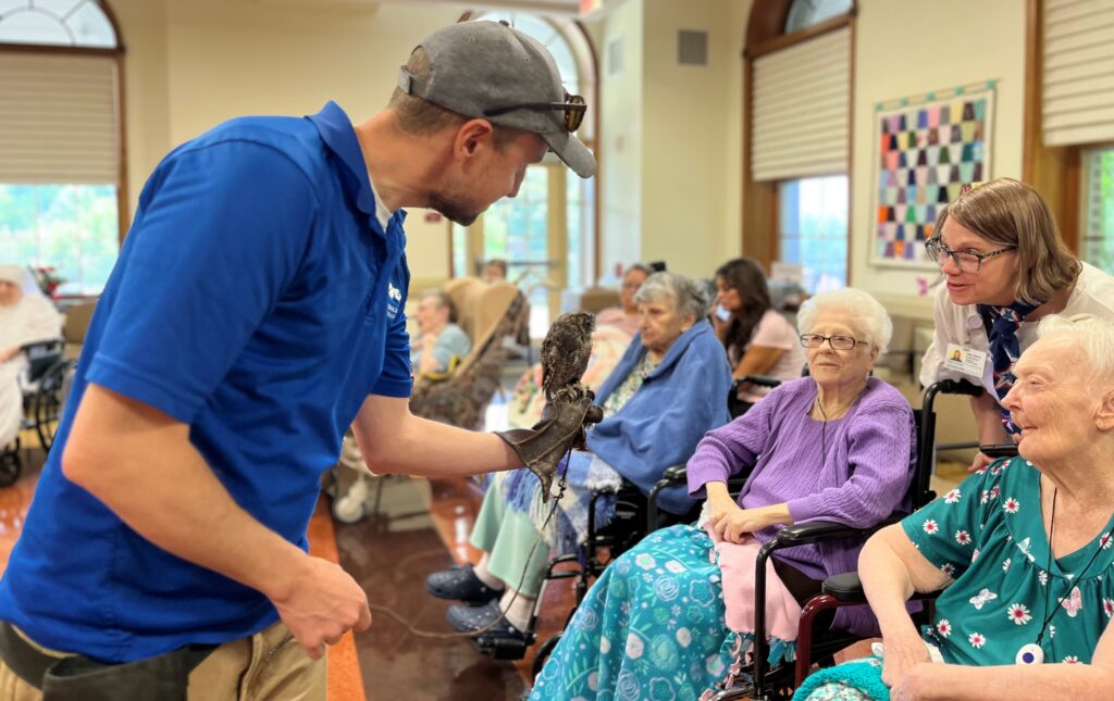 National Aviary expert, Mike Faix, holding an Eastern Screech-Owl on his gloved hand as adult learners look on in excitement