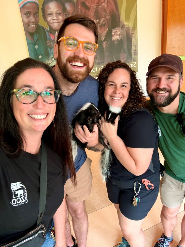 Jake holding one skunk and posing with trainers at the Cincinnati Zoo